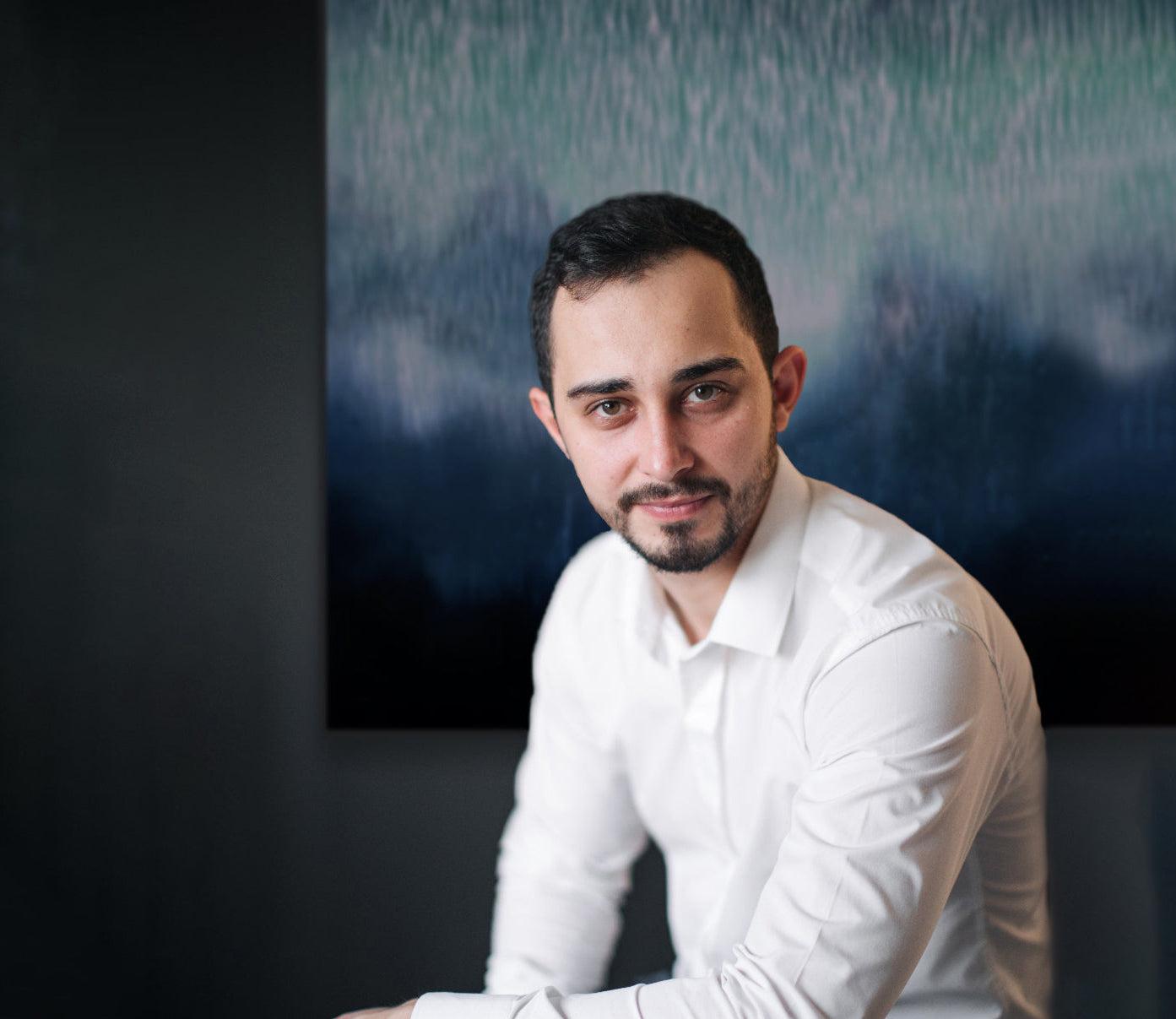 Man in a white shirt sitting in front of an abstract painting